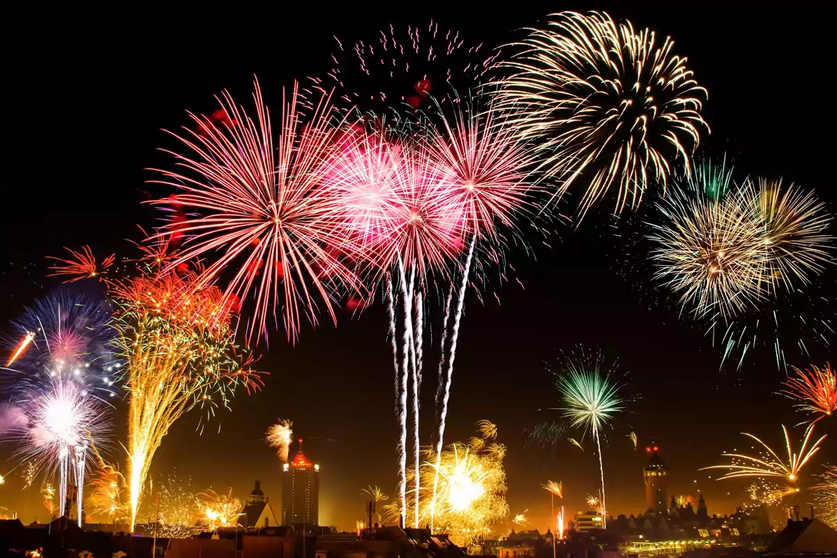 Fuegos artificiales multicolores iluminan el cielo nocturno sobre una ciudad.