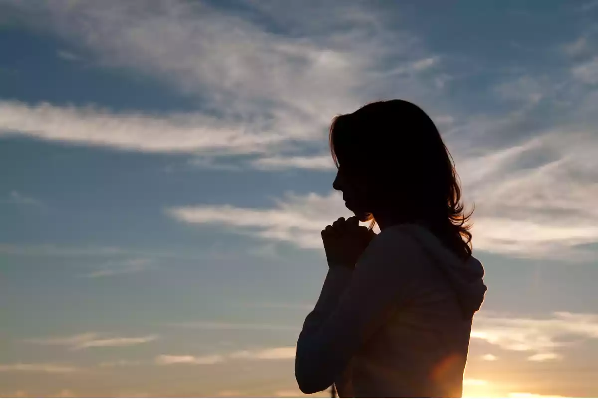 Persona en silueta rezando al atardecer con el cielo nublado de fondo.