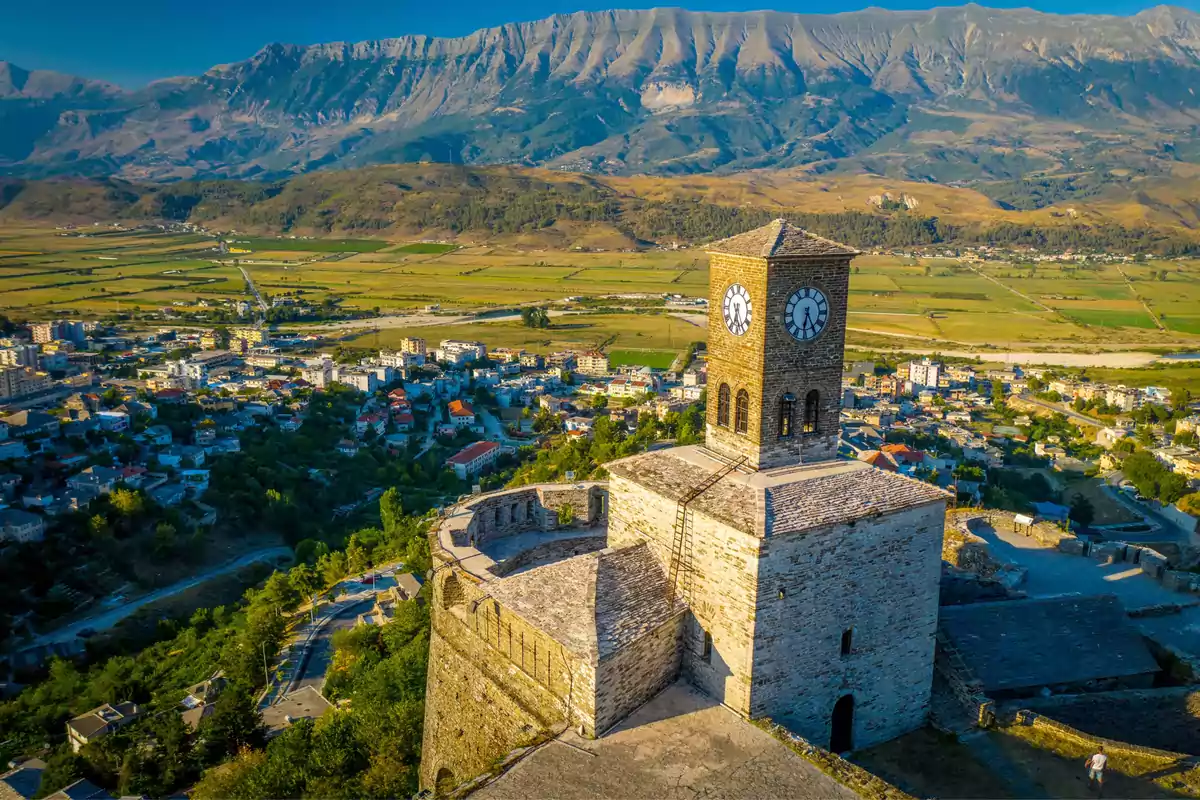 Vista aérea de una torre de reloj en una ciudad con montañas al fondo.